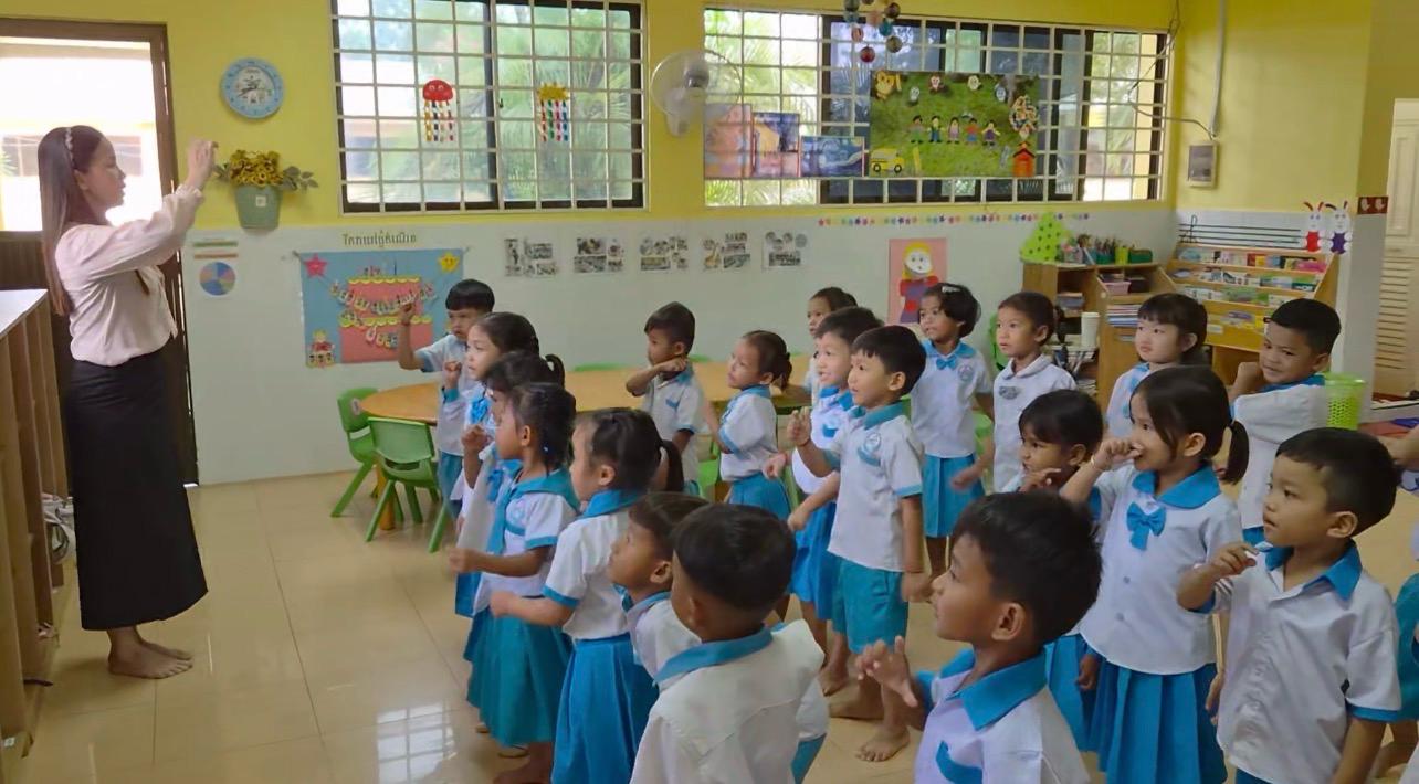 Children in blue-and-white uniforms gathered with their teacher at Bethel School, Cambodia