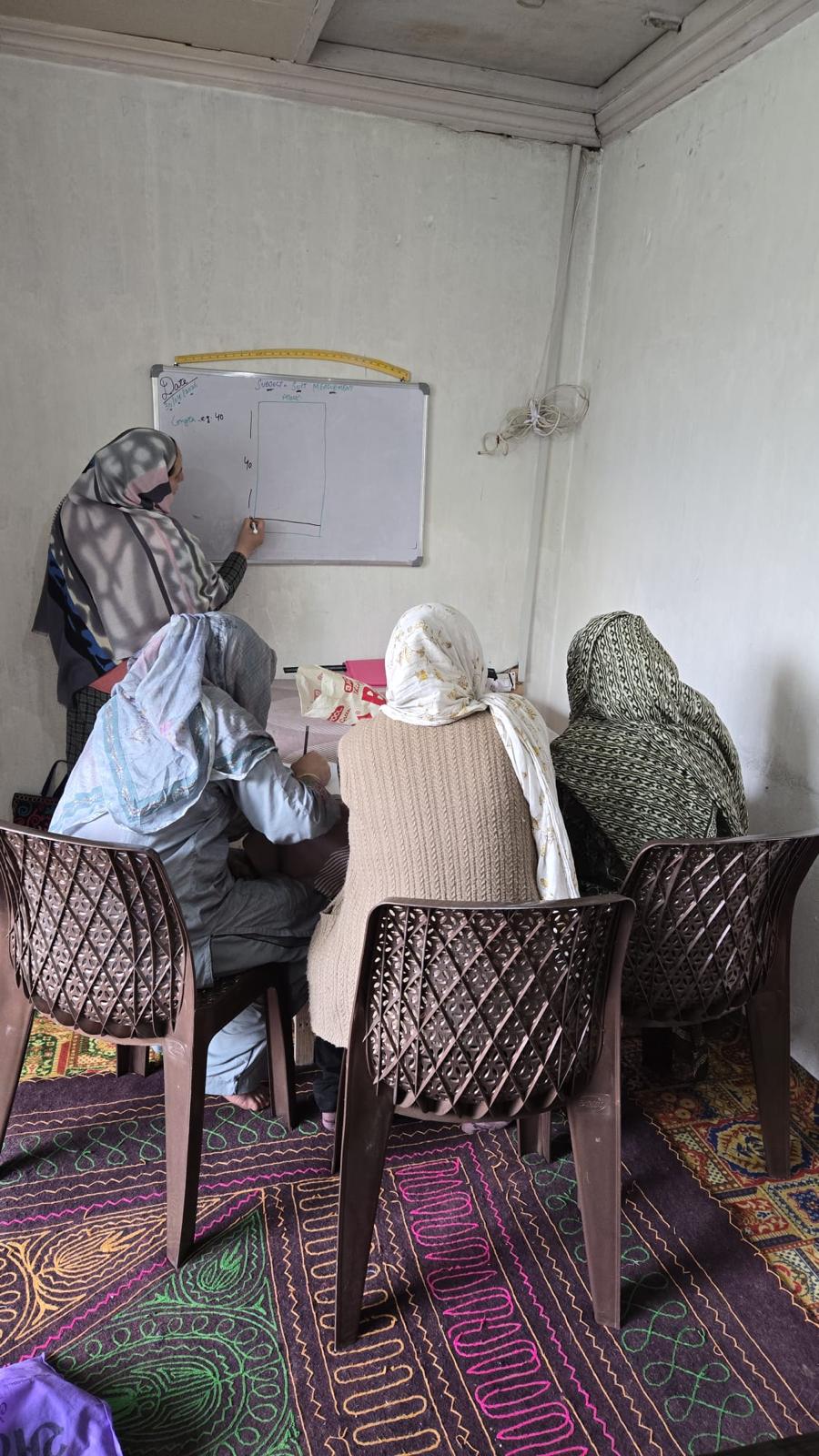 FDSS instructor teaching sewing measurements at a whiteboard to three women students in India